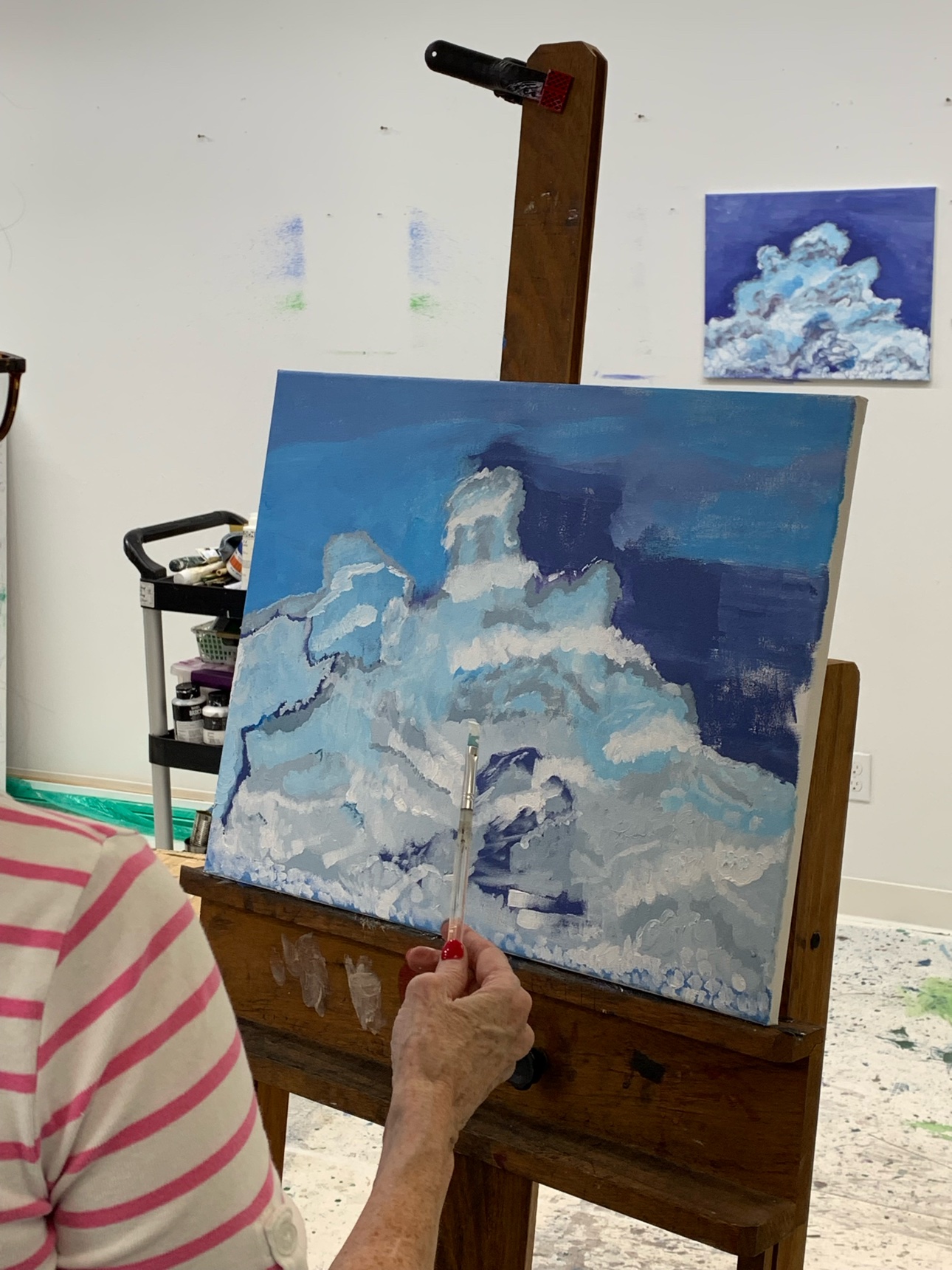 A student painting clouds in acrylic on an easel. Acrylic holds bold color and lets you paint over a layer once it dries.