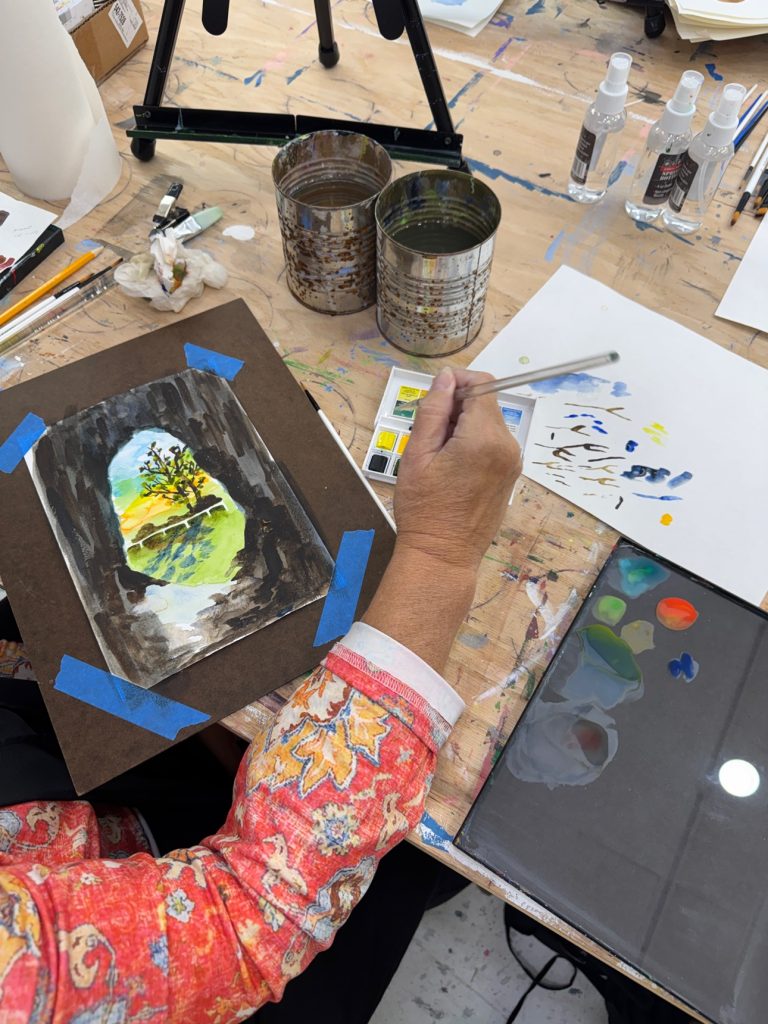 A student working on a watercolor in class, with guidance while the painting can still change.