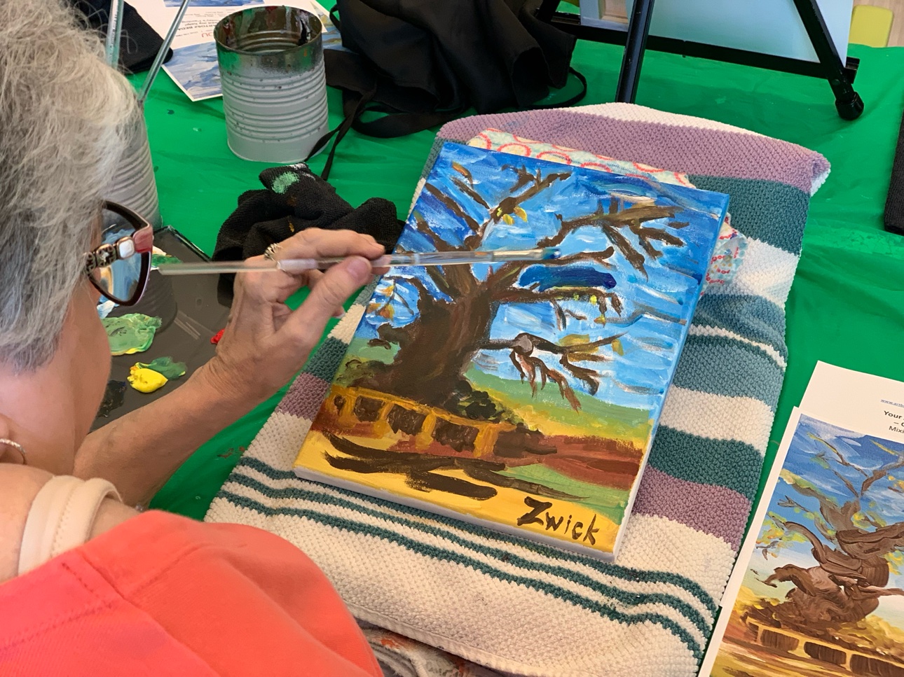 A resident painting a tree step by step, with the printed instruction sheet beside the canvas.